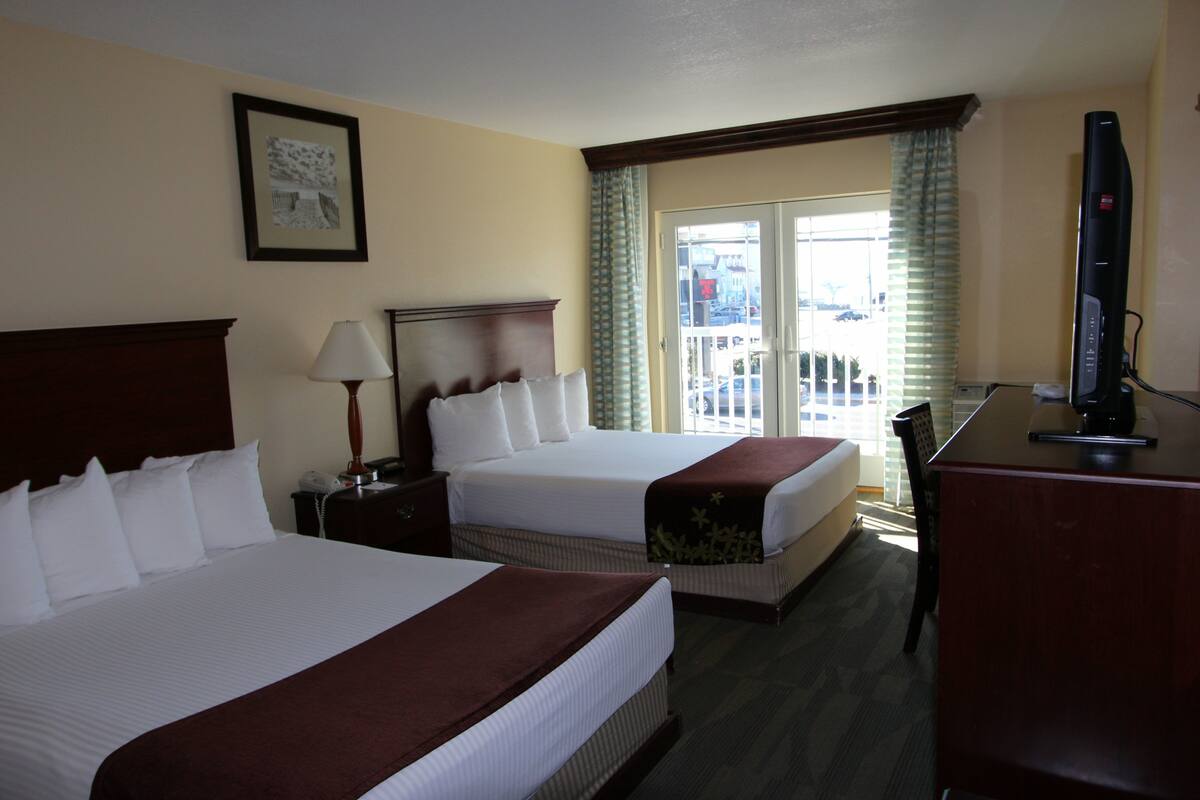 Een hotelkamer met twee bedden, een bureau, een televisie en een balkon met uitzicht.