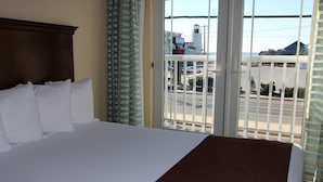 A hotel room with a large bed, a view of the parking lot, and a cityscape in the background.