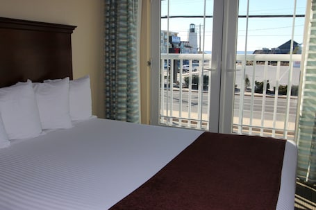 Habitación de hotel con una cama grande, vista al estacionamiento y un paisaje urbano al fondo.