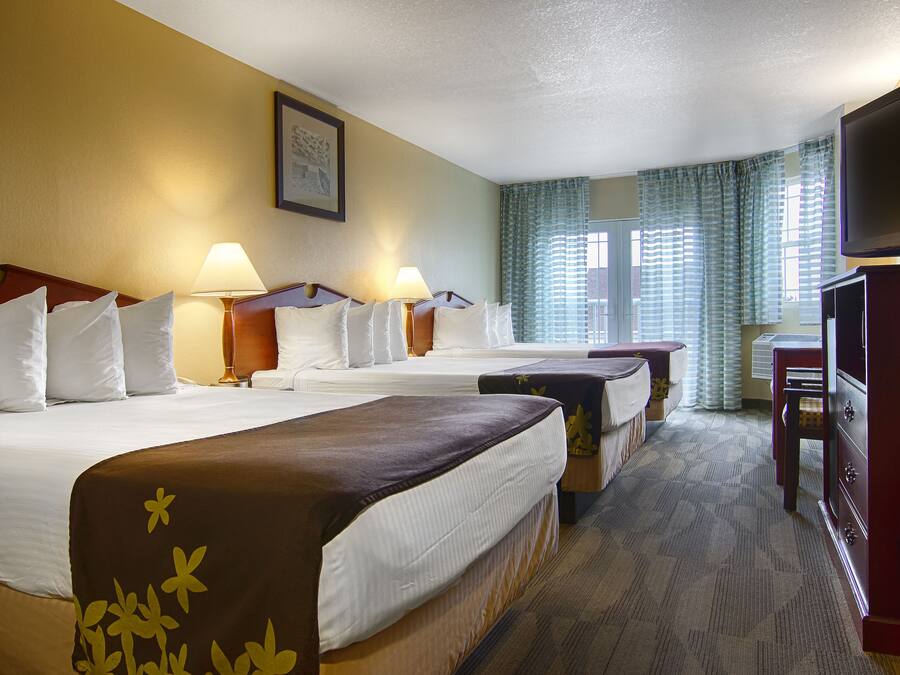 Habitación de hotel con dos camas, televisión, escritorio y ventana con cortinas.