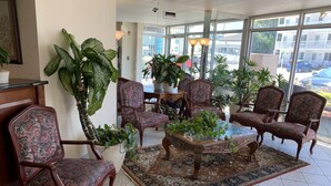 Un hall d’entrée spacieux, doté d’une grande fenêtre, de plusieurs fauteuils ornés de motifs floraux, d’une table basse centrale et d’une variété de plantes en pot.