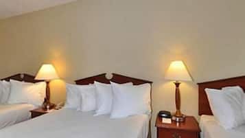 Habitación de hotel con dos camas, cada una con sábanas blancas y cabeceros de madera. Hay dos mesitas de noche, una de ellas con una lámpara y un reloj pequeño.