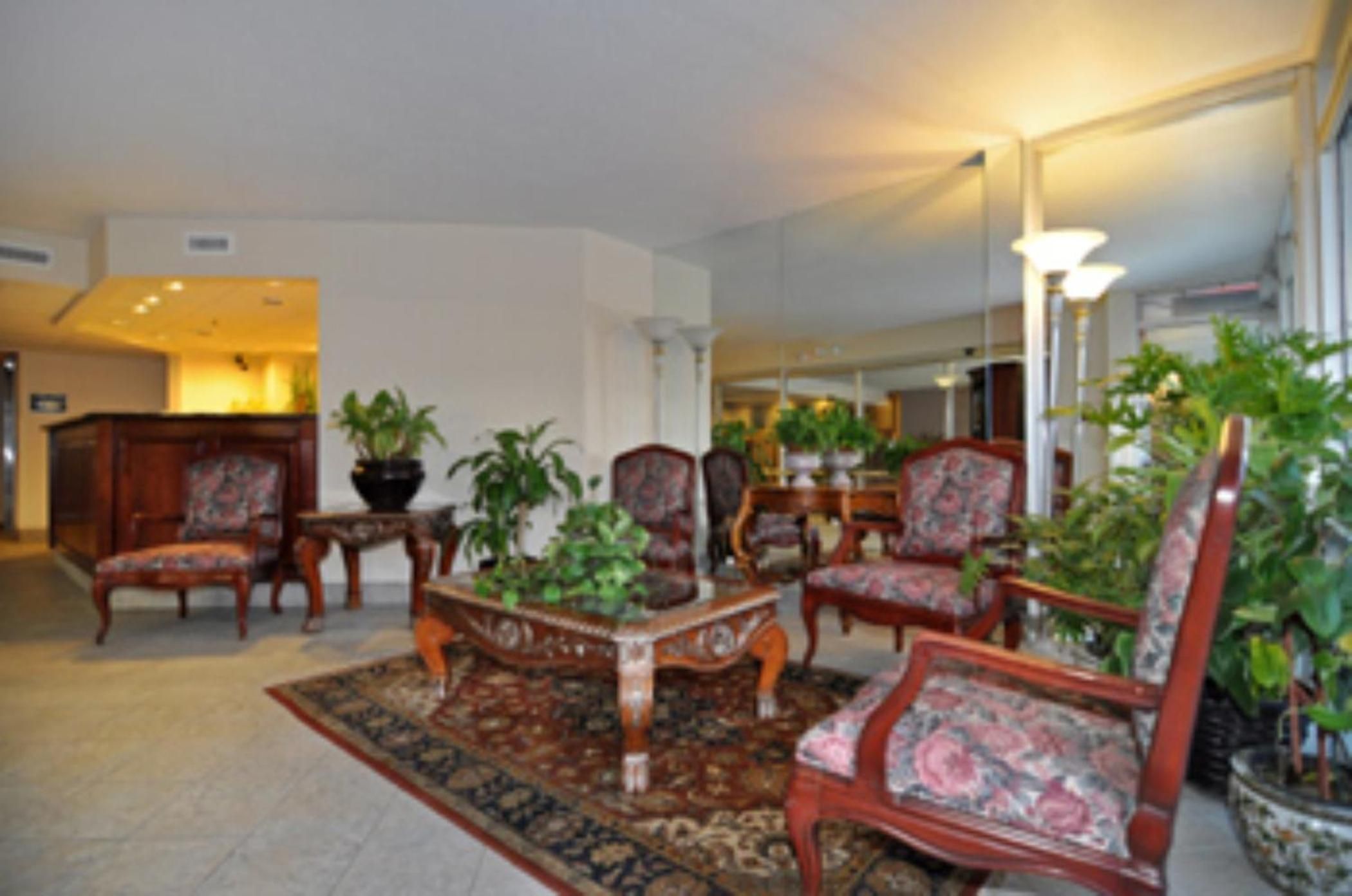 A lobby with a reception desk, several chairs, a coffee table, and potted plants.
