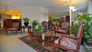 Un hall con mostrador de recepción, varias sillas, una mesa de centro y plantas en macetas.