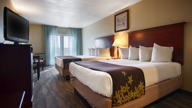A hotel room with two beds, a desk, a television, and a window with curtains.
