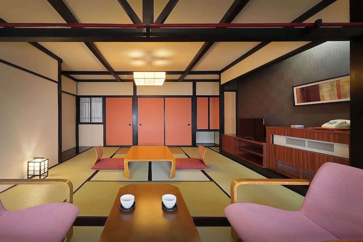 Una habitación japonesa tradicional con suelo de tatami, una mesa baja con dos cuencos y un televisor sobre un mueble de madera.