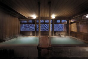 Un balneario tradicional de madera con dos tinas de hidromasaje, paredes de piedra y techo de madera.