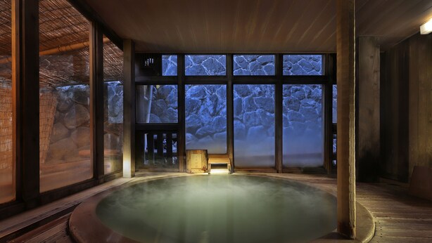 A hot tub with a stone wall backdrop and a wooden floor. - Omiya Ryokan (Yamagata)