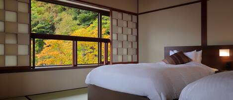 Ein traditioneller japanischer Raum mit Tatami-Boden, einem großen Fenster mit Blick auf Herbstlaub und einem Bett mit weißer Bettwäsche.