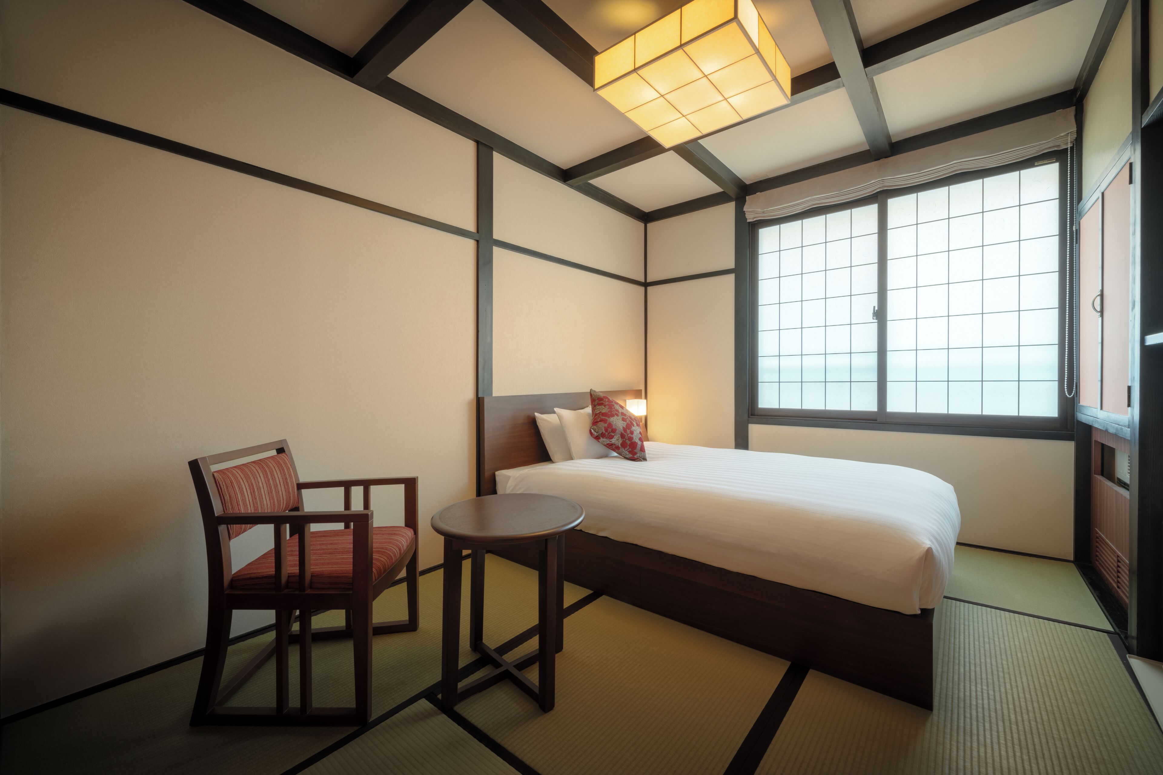 A traditional Japanese-style room with tatami flooring, a low wooden bed, a small table, and a chair.