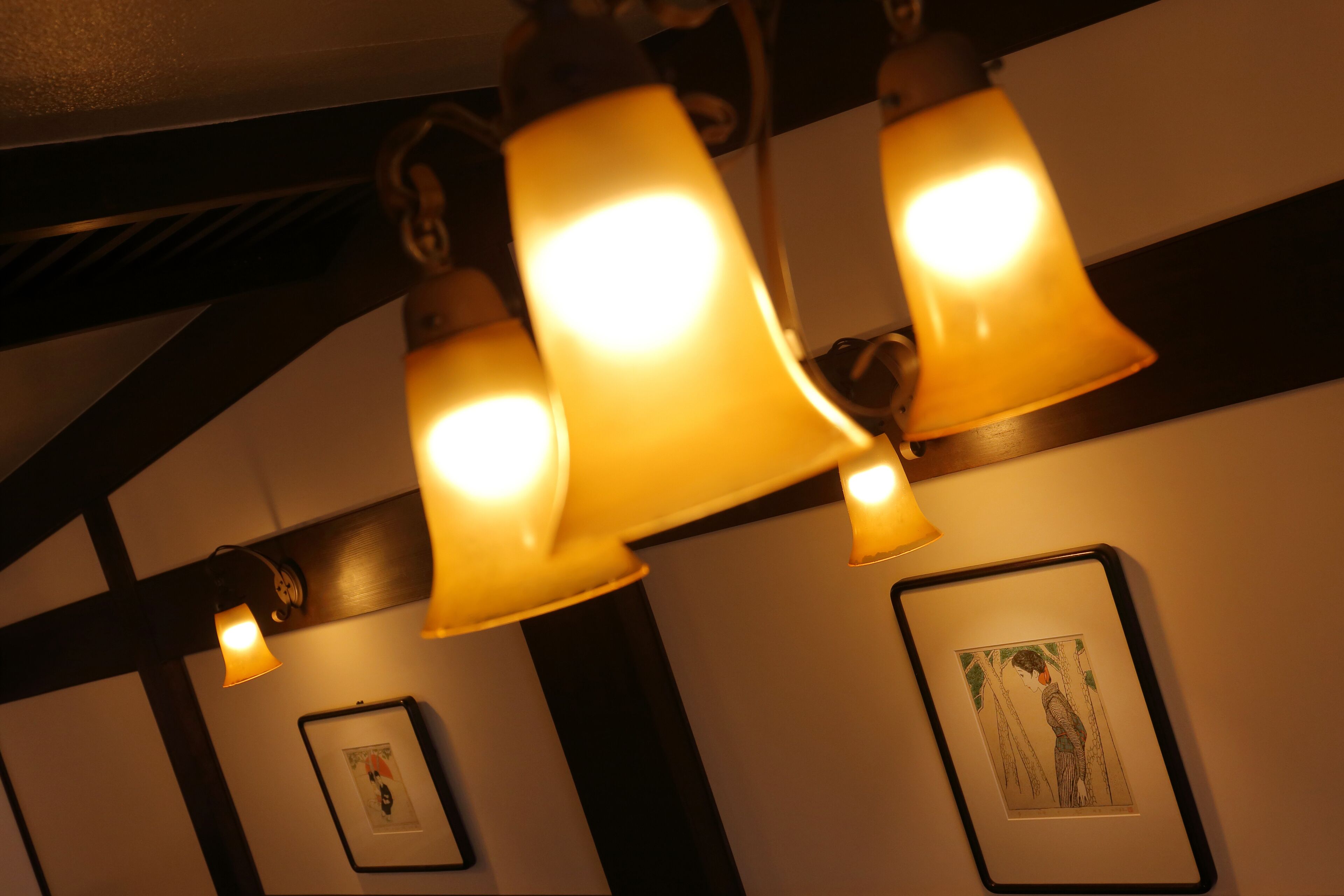 A ceiling with three illuminated fixtures and two framed pictures on the wall.