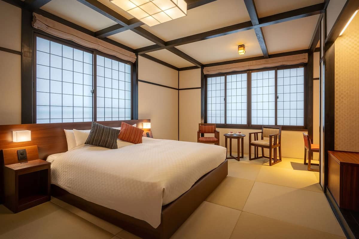 A hotel room with a large bed, bedside tables, a desk with chairs, and a television.