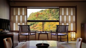 A traditional Japanese room with tatami flooring, a low table with a bowl, two chairs, and a view of autumn foliage through a shoji screen. - Omiya Ryokan (Yamagata)