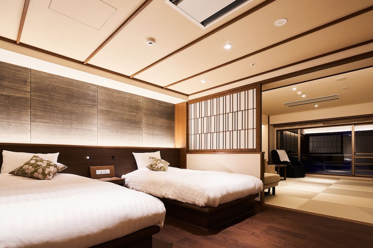 Una habitación de hotel moderna con dos camas, suelo de madera, un ventanal grande y una puerta corredera que da a un balcón.