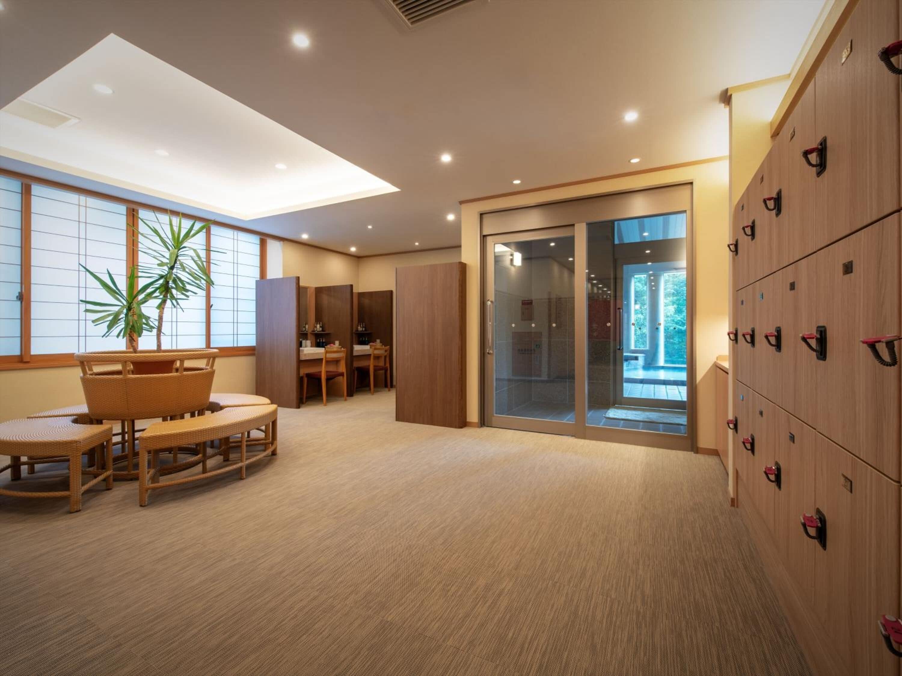A hotel room with a large sliding glass door, a wooden cabinet with hooks, a dining area with a table and chairs, and a large window with a view of the outdoors.