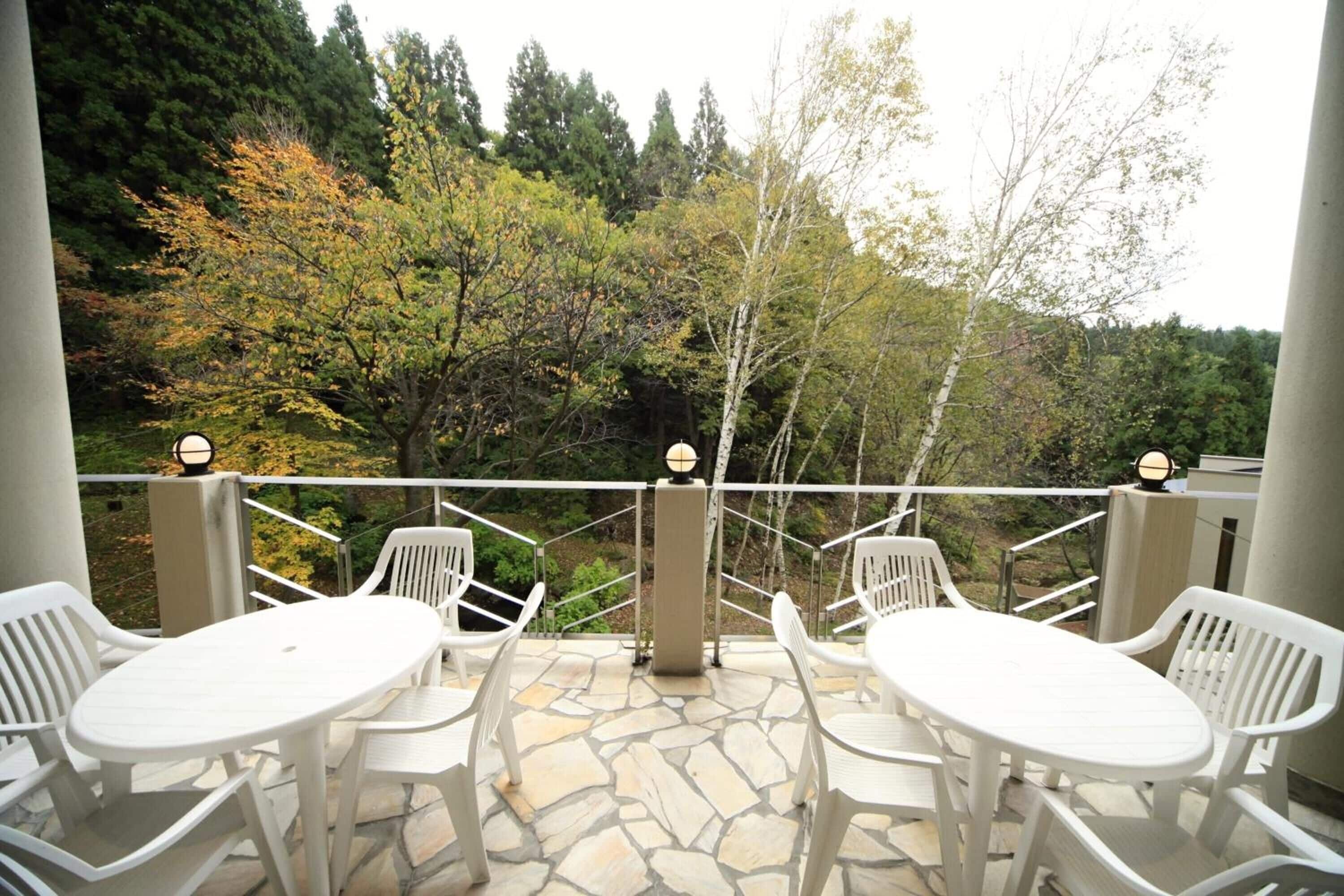 An outdoor patio with white plastic chairs and a table, surrounded by a stone floor and a white railing.