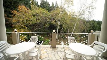 An outdoor patio with white plastic chairs and a table, surrounded by a stone floor and a white railing.