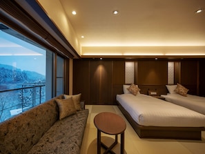 Quarto de hotel moderno com uma cama grande, um sofá, uma mesinha e vista para uma paisagem nevada.
