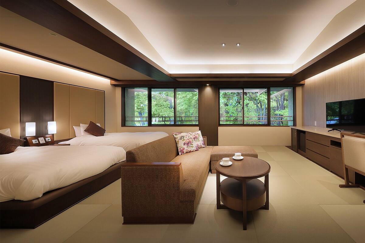A modern hotel room with two beds, a sofa, a desk, and a TV.