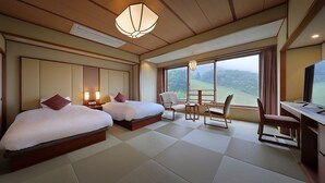 Habitación de hotel con dos camas, un escritorio, una silla y un ventanal con vistas al exterior.