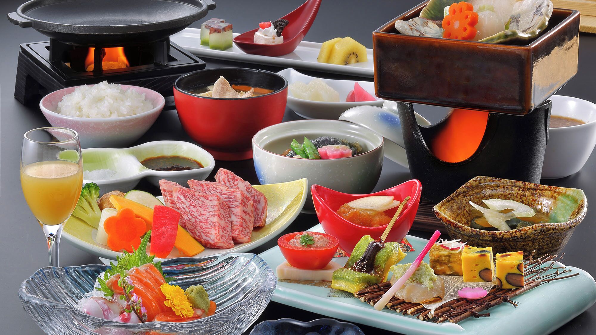 A variety of Japanese dishes including sushi, sashimi, and tempura, served on a table with a teapot and cups.