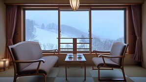 Una habitación con dos sillas y una mesa, ventanas amplias que dan a un paisaje nevado.