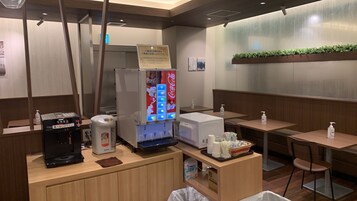 Una camera d'albergo con minibar, frigorifero, distributore automatico di Coca-Cola, macchina per il caffè e un piccolo cestino.