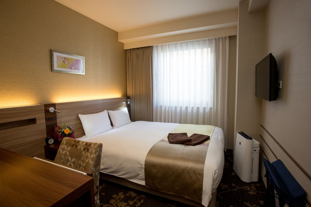 A hotel room with a bed, a desk, a chair, a TV, and a window with curtains.