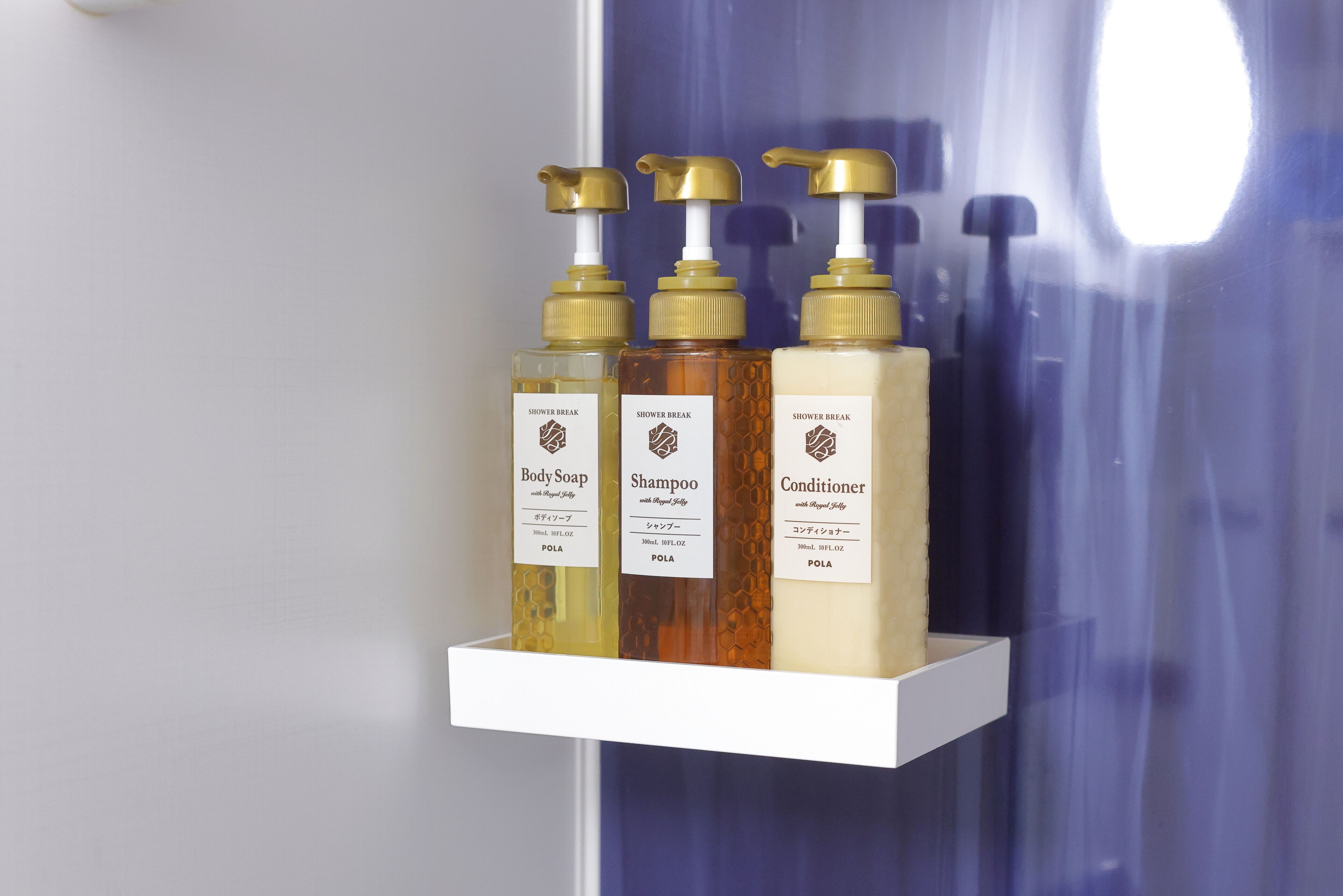 Three bottles of shower products on a white shelf.