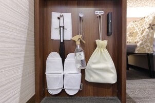 A hotel room with a wooden door, a pair of white slippers, a spray bottle, a white bag, and a hair dryer hanging on the wall.