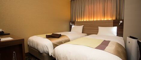A hotel room with two beds, a desk, and a trash bin.