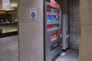 A vending machine with various drinks and snacks, a sign indicating a free room, and a glass door entrance.