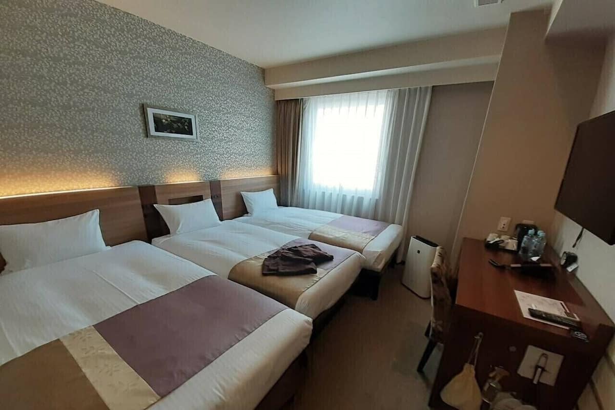 A hotel room with two beds, a desk, a chair, a TV, and a window with curtains.