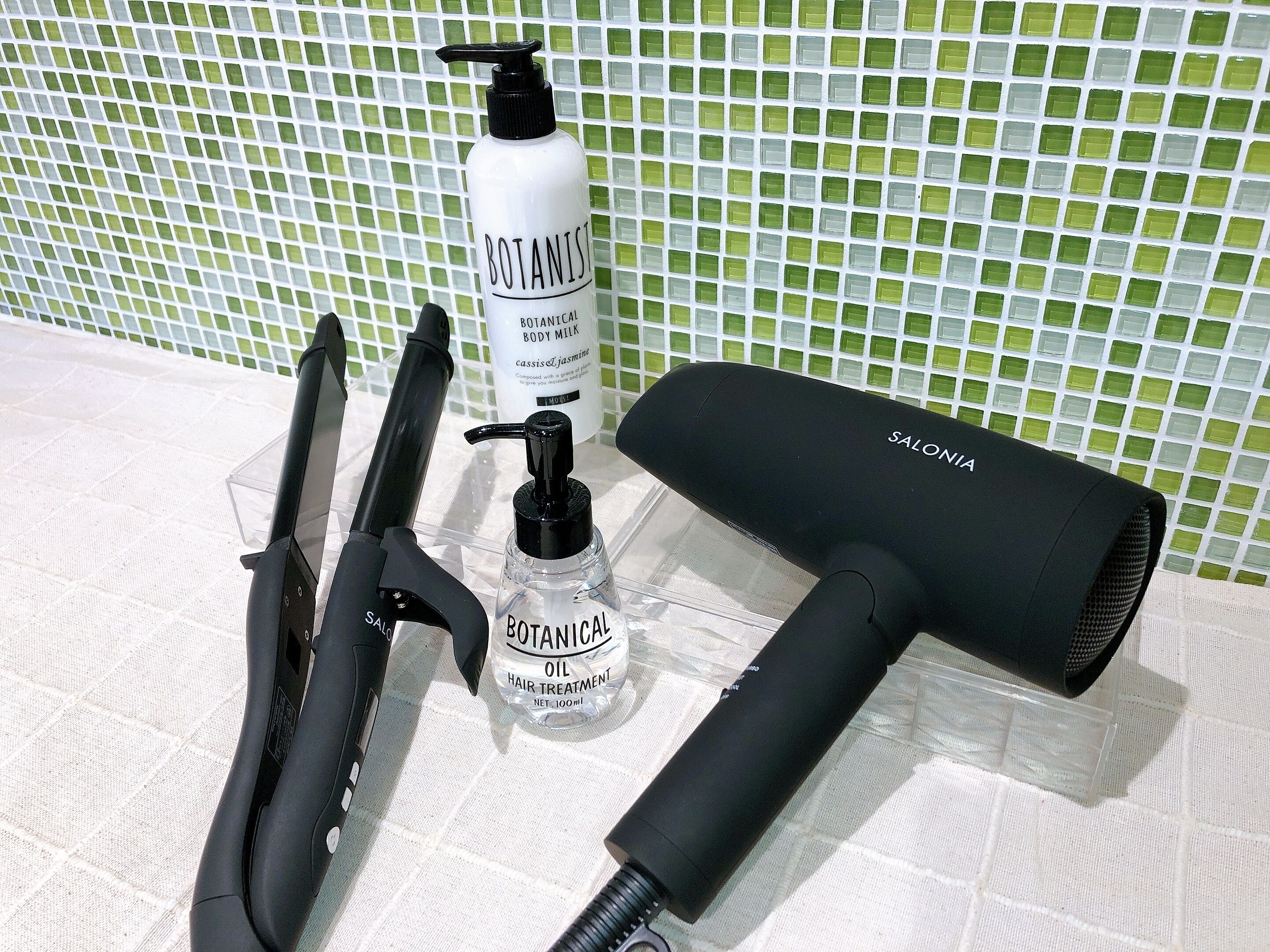 A hair styling station with a hairdryer, a hair clipper, a bottle of botanical body milk, and a bottle of botanical hair treatment oil.
