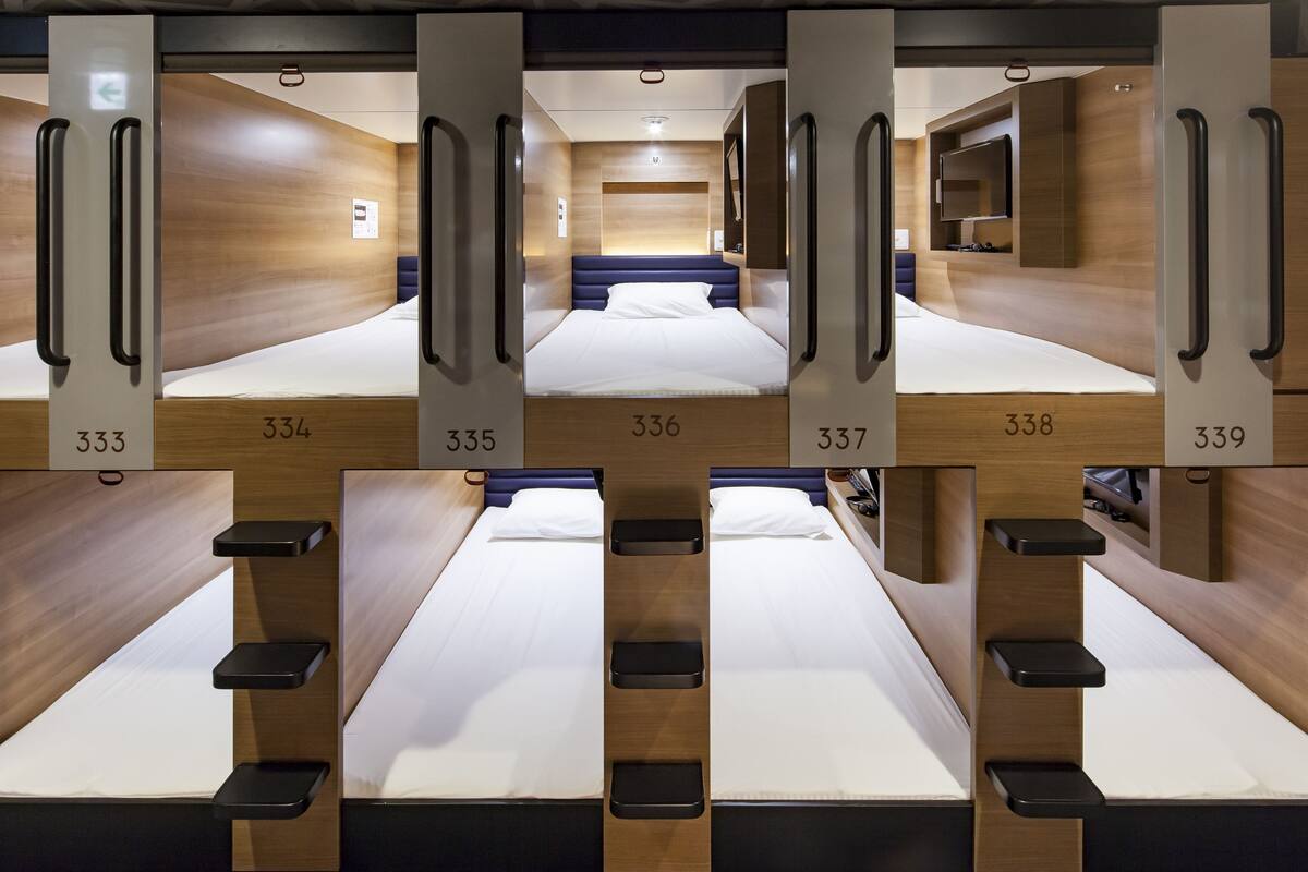 A modern hotel room with a central bed flanked by two smaller beds, each with a wooden headboard and a number above.