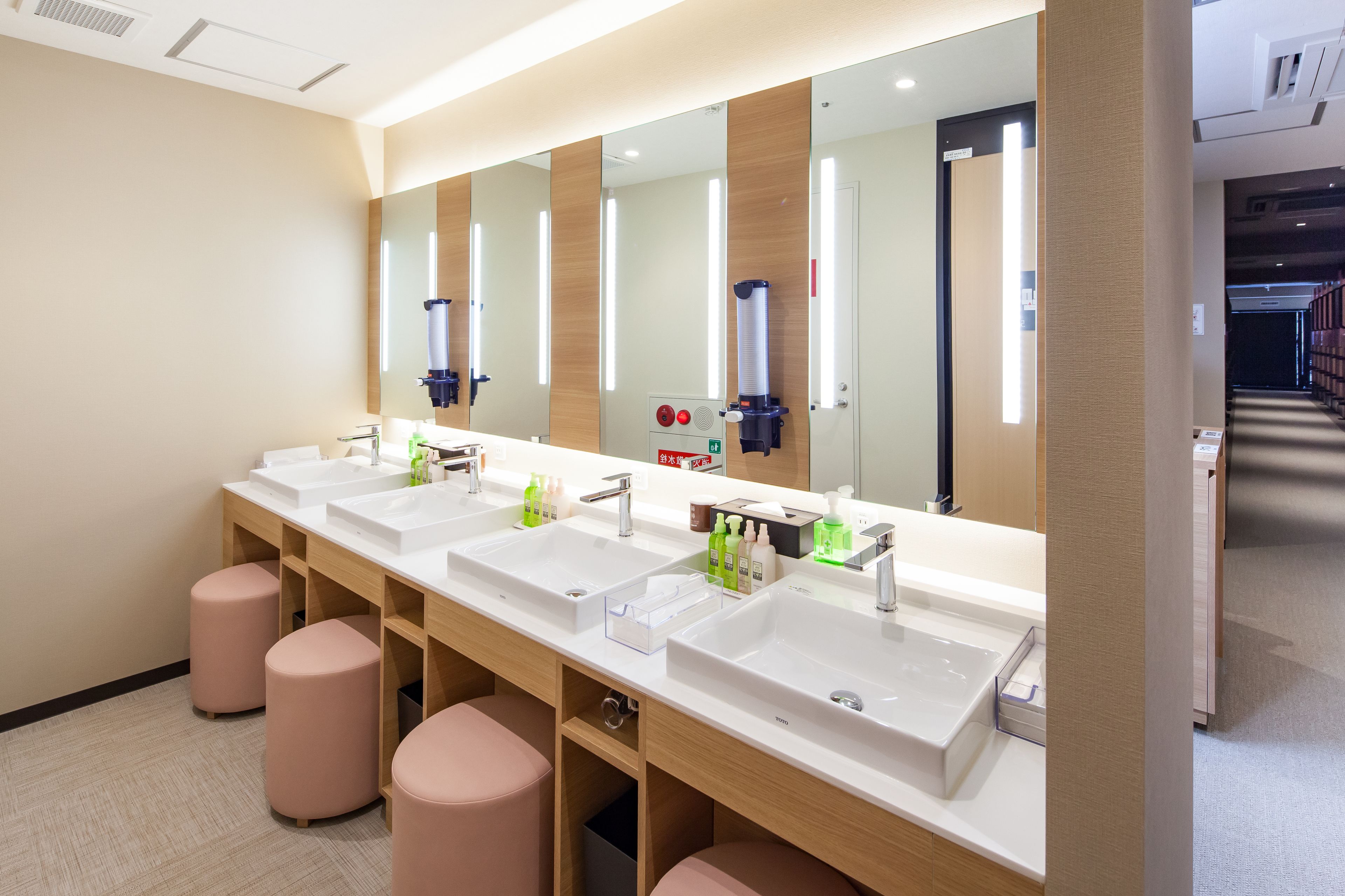 A modern bathroom with three sinks, a large mirror, and pink stools.