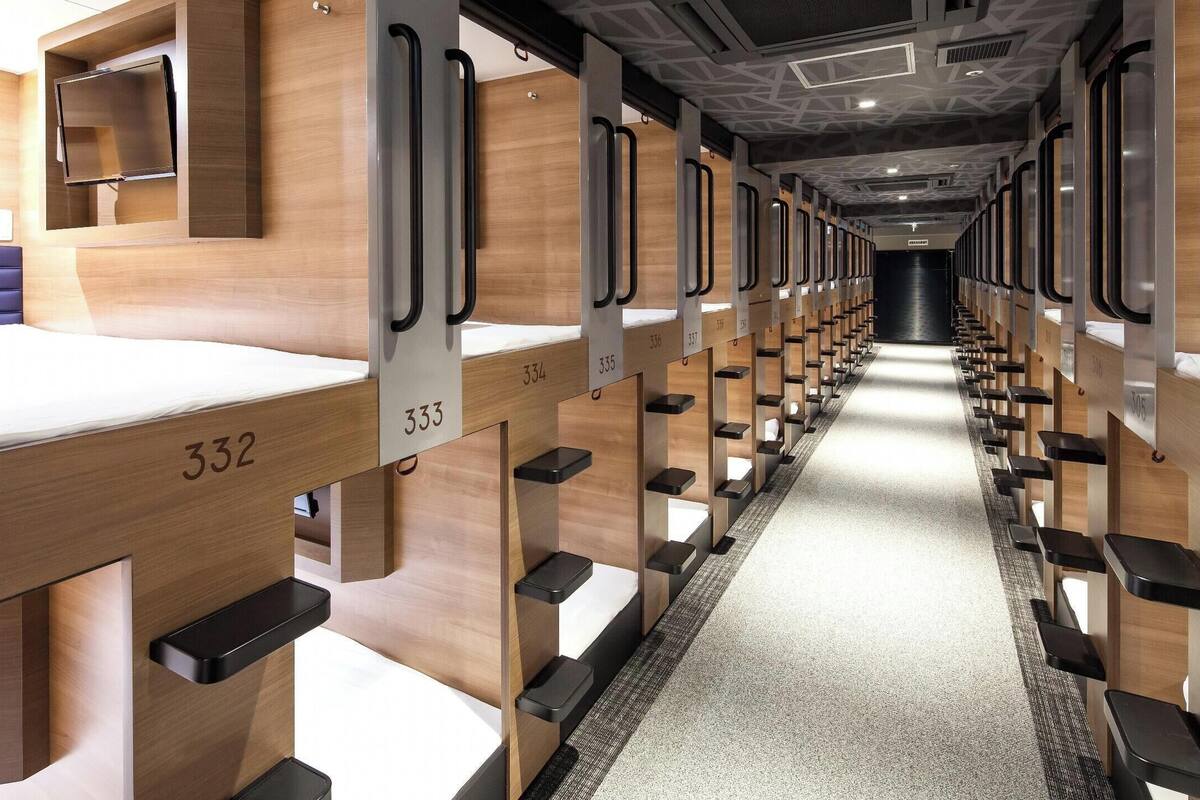 A modern hotel room with a wooden floor, a bed with a number, and a corridor with numbered compartments.