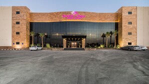 A modern hotel entrance with a large glass facade, palm trees, and a parking lot. - Boudl Al Munsiyah (Riyadh)