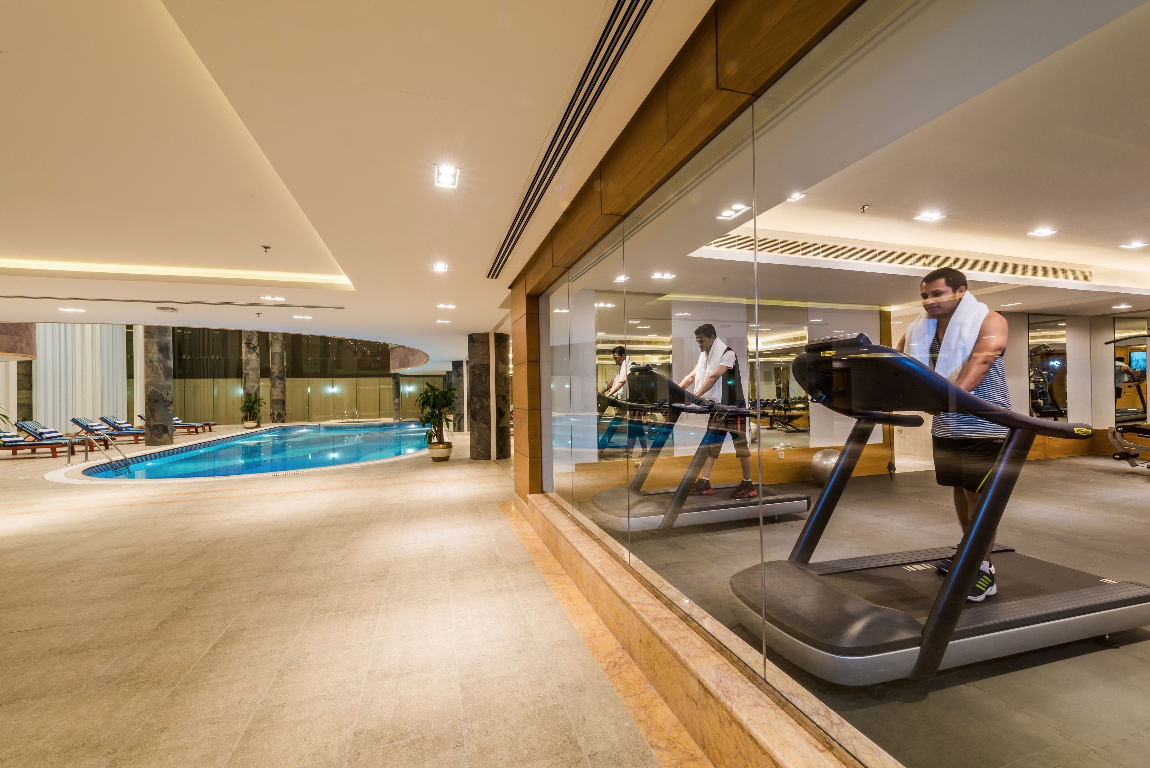A gym with a large indoor pool, exercise equipment, and a glass wall reflecting the interior.