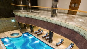 A large indoor swimming pool with a wavy design, surrounded by lounge chairs and a glass balustrade. - Boudl Al Munsiyah (Riyadh)