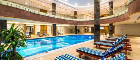 A multi-level indoor swimming pool with lounge chairs and a potted plant.