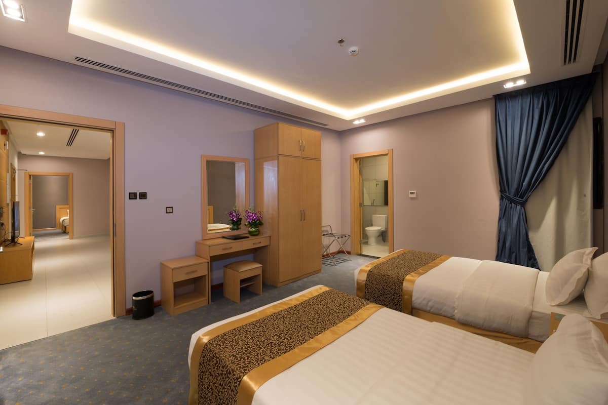 A modern hotel room with two beds, a desk, a wardrobe, and a bathroom.