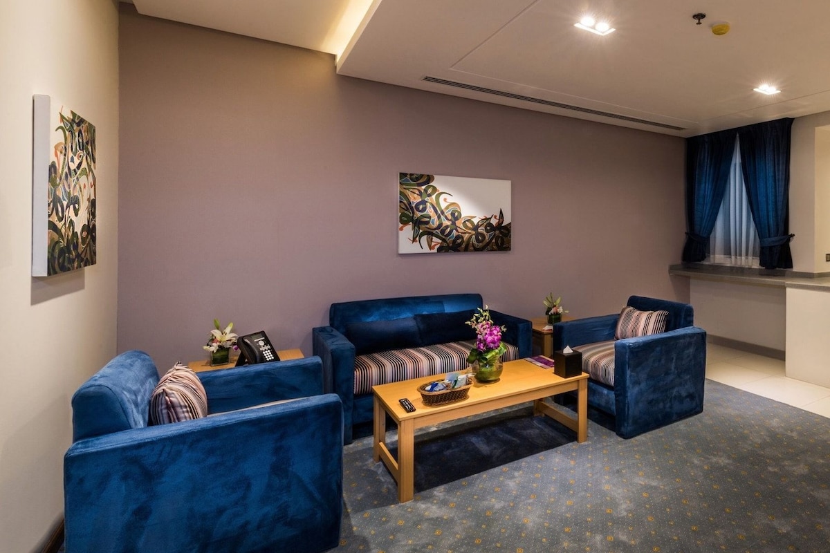 A modern living room with blue sofas, a wooden coffee table, and artwork on the walls.