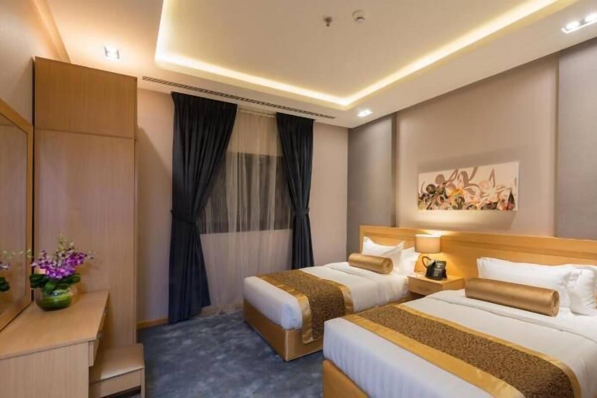 A hotel room with two beds, a desk, a mirror, and a painting on the wall.