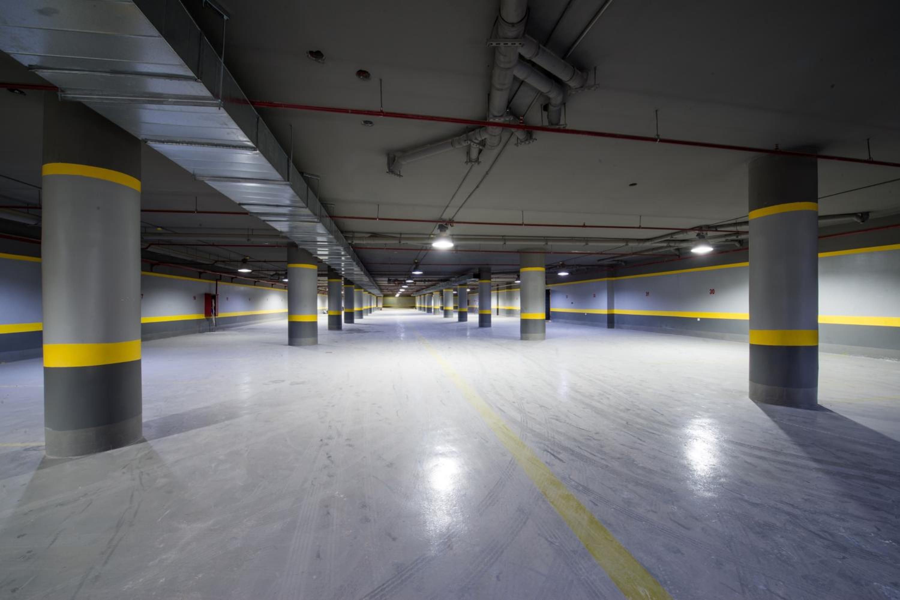 A multi-level parking garage with concrete pillars, yellow safety lines, and overhead pipes.
