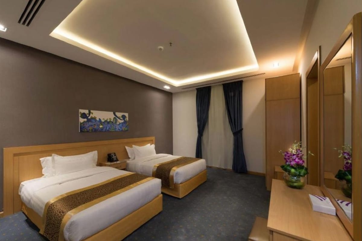 A hotel room with two beds, a desk, a mirror, and a painting on the wall.