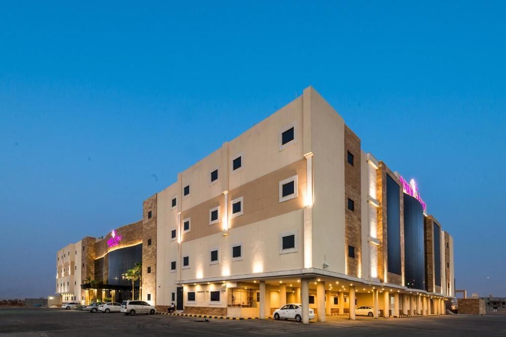 A multi-story hotel with a flat facade, multiple windows, and a parking area in front.