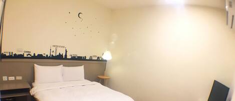 A hotel room with a bed, a nightstand, a small table, and a wall with a city skyline mural.