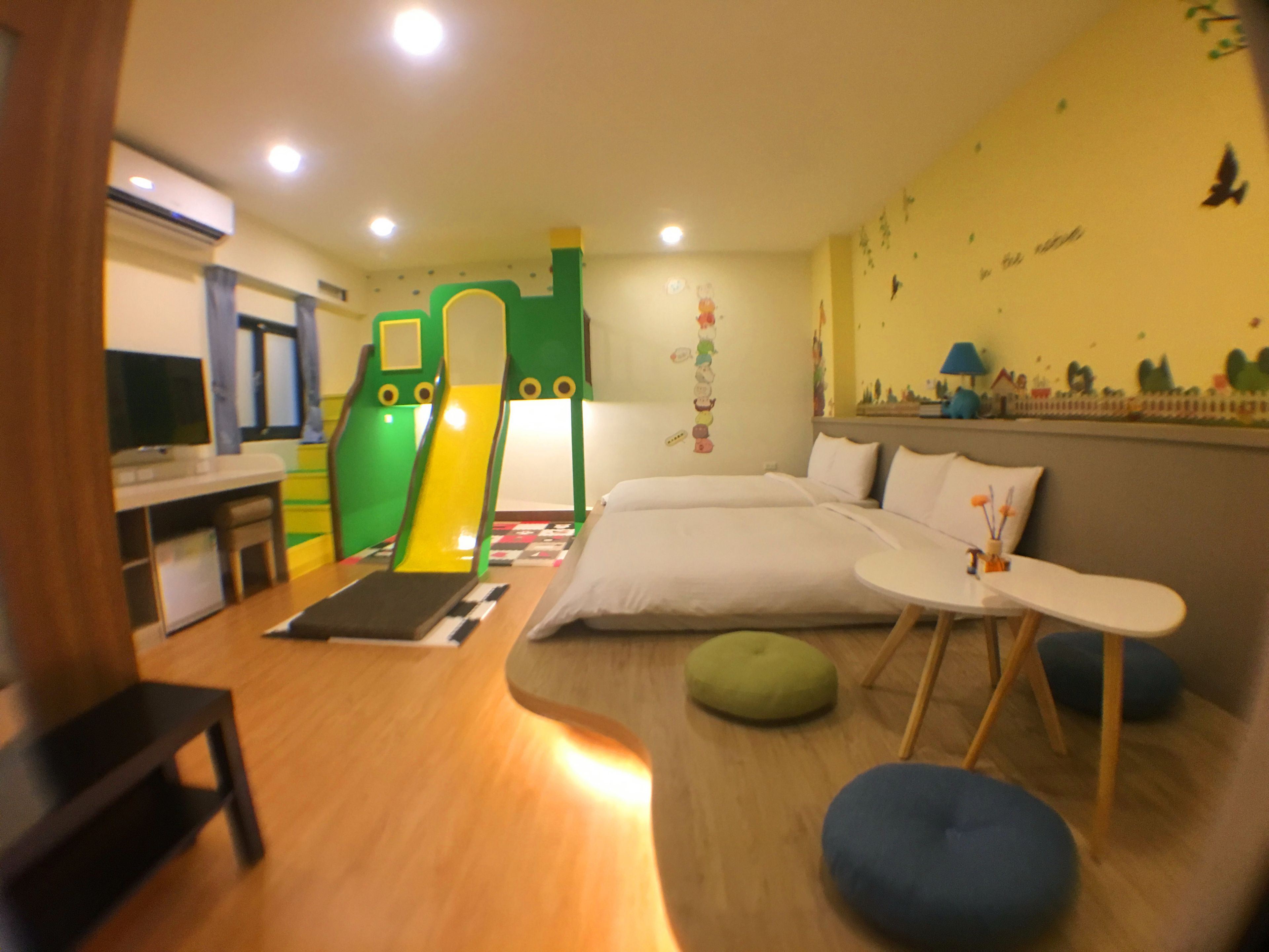 A child's play area with a slide and climbing structure, a bed with pillows, a small table, and a TV.