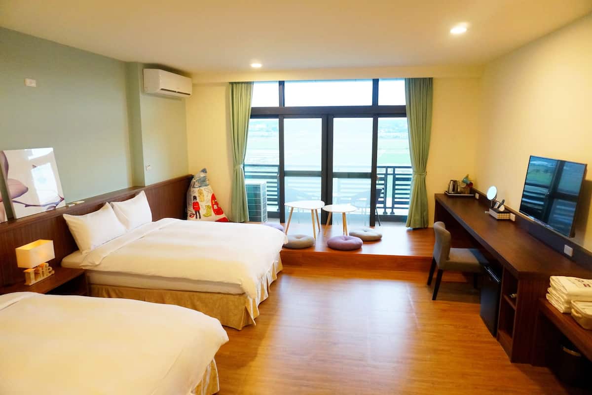 A hotel room with two beds, a desk, a chair, a TV, and a balcony with a view.